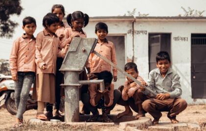 Ein Junge trinkt Wasser aus einer Wasserpumpe. Seine Freunde stellen sich für ein Foto auf.